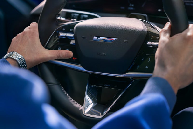 Close-up of a Man About to Press the V-Button on the 2026 OPTIQ-V Steering Wheel | Dan Vaden Cadillac Brunswick in Brunswick GA